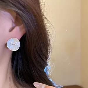 A detailed close-up showing the matte silver circular stud earrings with embossed horse