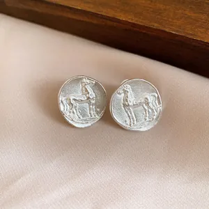 Close-up view of matte silver round stud earrings featuring a vintage embossed horse