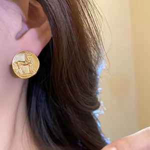 Close-up of matte gold round stud earrings featuring a vintage horse motif on ear