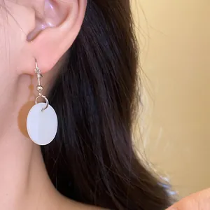 Close-up detail of an elegant white shell round pendant earring on a female ear.