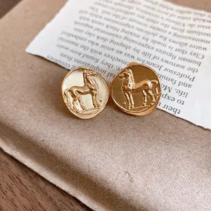Close-up of vintage matte gold round earrings featuring a detailed horse coin relief