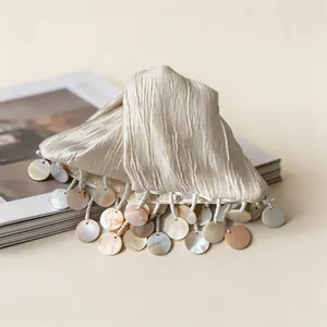 Detailed macro view of a cream fabric hair claw clip with iridescent shell disc tassels.