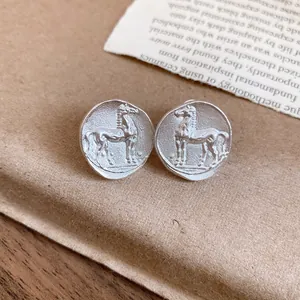Detailed macro view of matte silver horse coin stud earrings with vintage texture