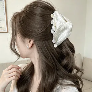 Elegant cream fabric hair claw clip with shell tassel detail shown on long hair