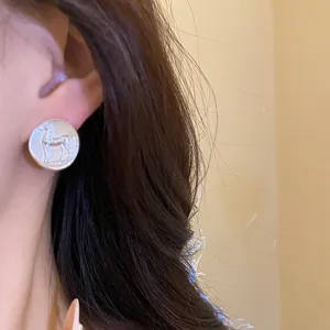 Detailed close-up of a matte silver round stud earring featuring an embossed horse design.