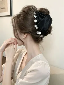 Detail of black satin hair claw clip with white shell tassels on model's bun hair.