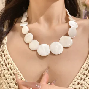 Close-up view of elegant white round shell disc necklace worn by model in crochet top