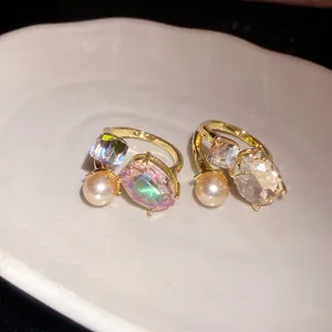 Macro view of gold open rings with oval faceted gemstones and pearls on a white dish