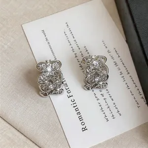 Détail des boucles d'oreilles en forme de C argentées avec motif fleur ajouré et strass