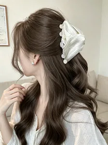 Elegant white ruffled fabric hair claw clip with shell tassels on wavy brown hair.