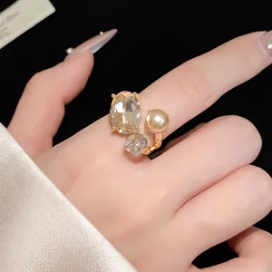 Detailed close-up of elegant open ring with oval crystal, pearl and gold finish.