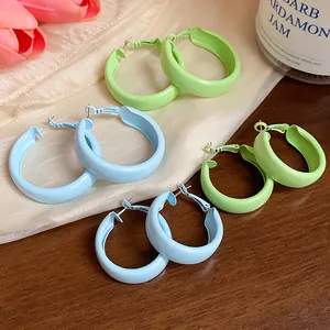 Close-up of pastel blue and green spray-painted hoop earrings on a soft fabric background