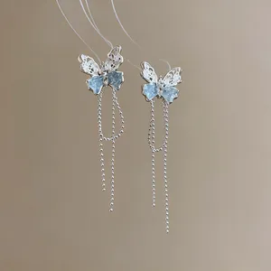 Detailansicht von silbernen Schmetterlingsohrringen mit blauen Flügeln und langen Quasten.