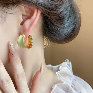 Dettaglio di un orecchino a cerchio minimalista in smalto verde chiaro e placcato oro 18 carati