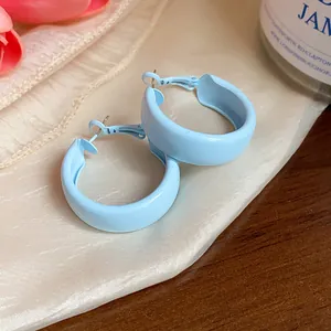 Detailed close-up view of light blue matte spray finish hoop earrings on elegant cream fabric