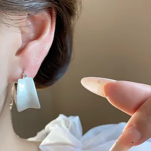 Primo piano di eleganti orecchini quadrati in smalto bianco placcati in oro 18 carati.
