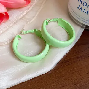Close-up view of minimalist mint green painted hoop earrings displayed on silk fabric