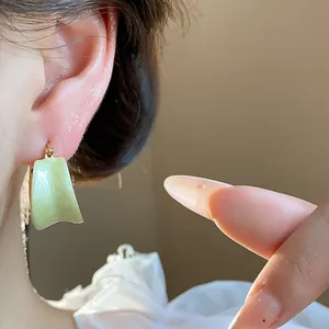 Dettaglio di orecchini in smalto verde chiaro placcati in oro 18 carati indossati su un orecchio