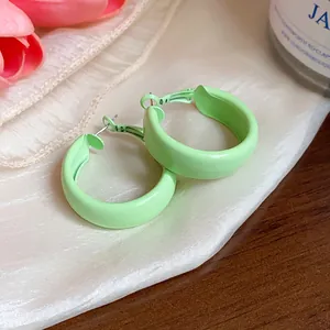 Detailed view of mint green spray-painted hoop earrings resting on soft silk fabric