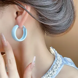 Close-up view of light blue spray-painted thick hoop earrings worn by a female model