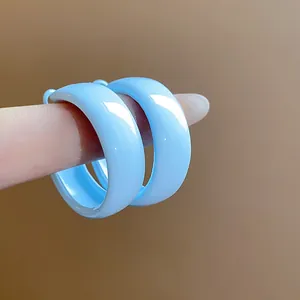Detailed close-up of light blue enamel hoop earrings with a glossy finish on finger