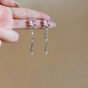 Boucles d'oreilles élégantes avec cœur rose, nœud et pompons sur fond neutre chic.