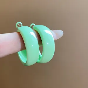 Close-up of mint green glossy hoop earrings held on a finger