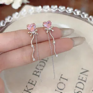 Vue détaillée d'élégantes boucles d'oreilles cœur rose avec nœuds et pompons argentés