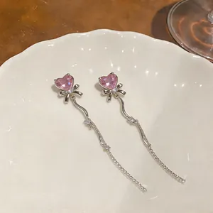 Vue détaillée des boucles d'oreilles élégantes avec cœur rose, nœud et pompons en cristal.