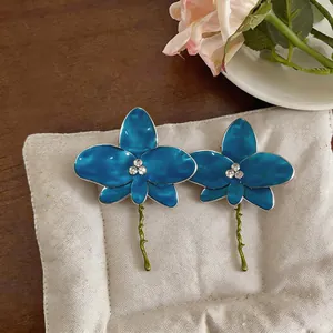 Detailed view of luxury blue enamel orchid earrings with sparkling rhinestones on a beige pad