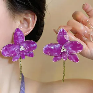 Close-up of purple enamel orchid earrings with rhinestone centers and gold stems