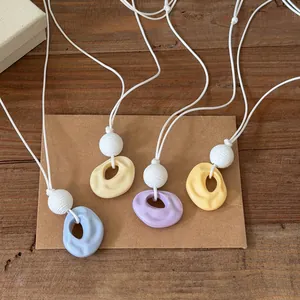 Detail view of four resin wrinkled ring necklaces in pastel colors with white cord straps