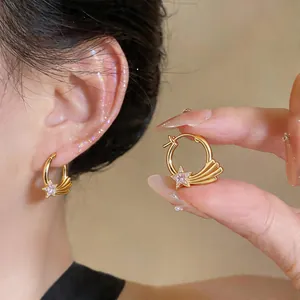 Detail von goldfarbenen Stern-Creolen mit Zirkonia, am Ohr getragen und in der Hand