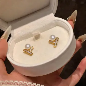 Elegant gold-tone stud earrings with pearls and zircons inside a white jewelry box.