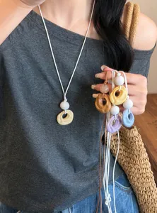 Close-up of colorful pleated resin pendants on white cord strings worn by a model