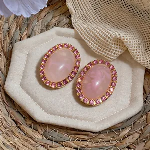 Elegant pink oval acrylic stud earrings with sparkly rhinestone halo in gold-tone setting