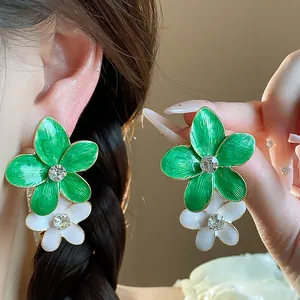 Dettaglio degli orecchini a fiore in smalto verde e bianco con strass scintillanti.