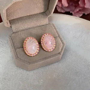 Elegant pink acrylic oval stud earrings with shimmering rhinestone halo in jewelry box