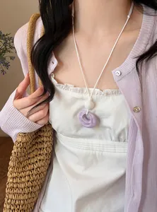 Detail of a purple resin pleated circular pendant necklace on a white leather-style cord.