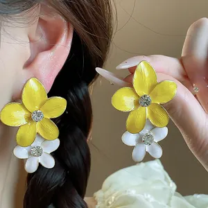 Primo piano di orecchini a fiore in smalto giallo e bianco con strass scintillanti.