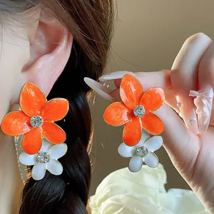 Primo piano di orecchini a fiore arancione e bianco con centri in cristallo scintillante.
