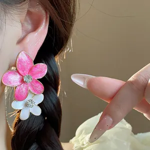 Primo piano di orecchini a fiore in smalto rosa e bianco con strass sull'orecchio