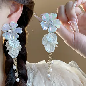 Close-up of iridescent acrylic flower earrings featuring pearls and gold tassels on a silver needle