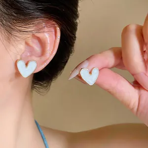Detailansicht der eleganten weißen Herz-Ohrstecker mit edlem goldenem Wellenrand-Design.