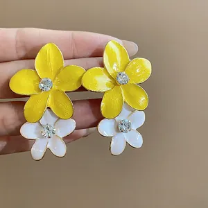 Dettaglio di orecchini a fiore in smalto giallo e bianco con un centro in strass luccicante