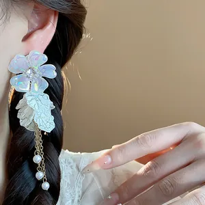 Close-up of elegant acrylic flower drop earrings with white pearl tassels on model