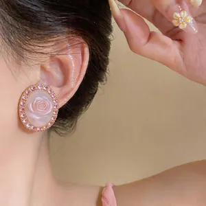 Close-up of elegant pink rose oval stud earrings with rhinestone borders on ear