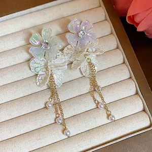 Macro detail of iridescent acrylic flower stud earrings with gold chains and pearls