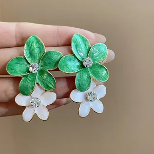 Dettaglio di orecchini a lobo a fiore in smalto verde e bianco con strass al centro