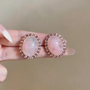 Close-up of elegant pink oval acrylic stud earrings with a purple rhinestone border.